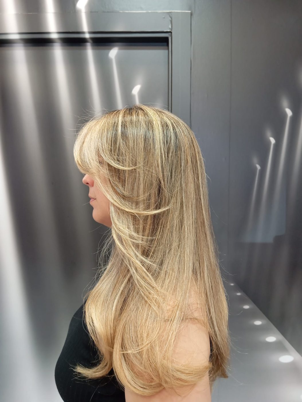 Melena rubia a capas con flequillo y ondas, vista de perfil